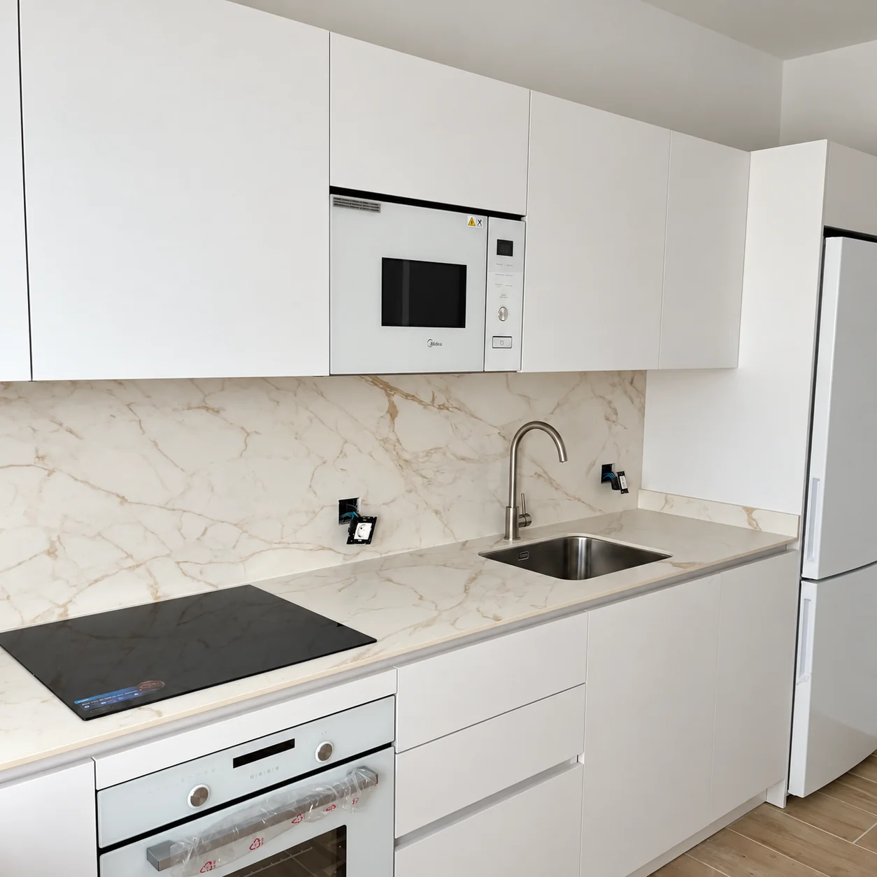 Cocina blanca con encimera veteada y electrodomésticos integrados