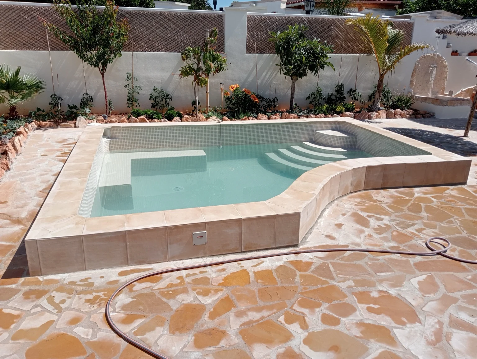Piscina con escalones de acceso, banco interior y terraza de piedra